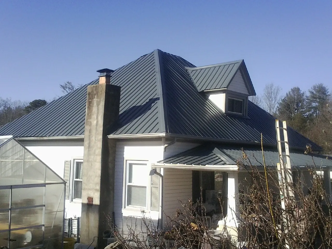 Dark blue standing seam metal roof on a white farmhouse with dormer — Slate & Tile Roof Repair by Roofing Brothers in Dunsmuir