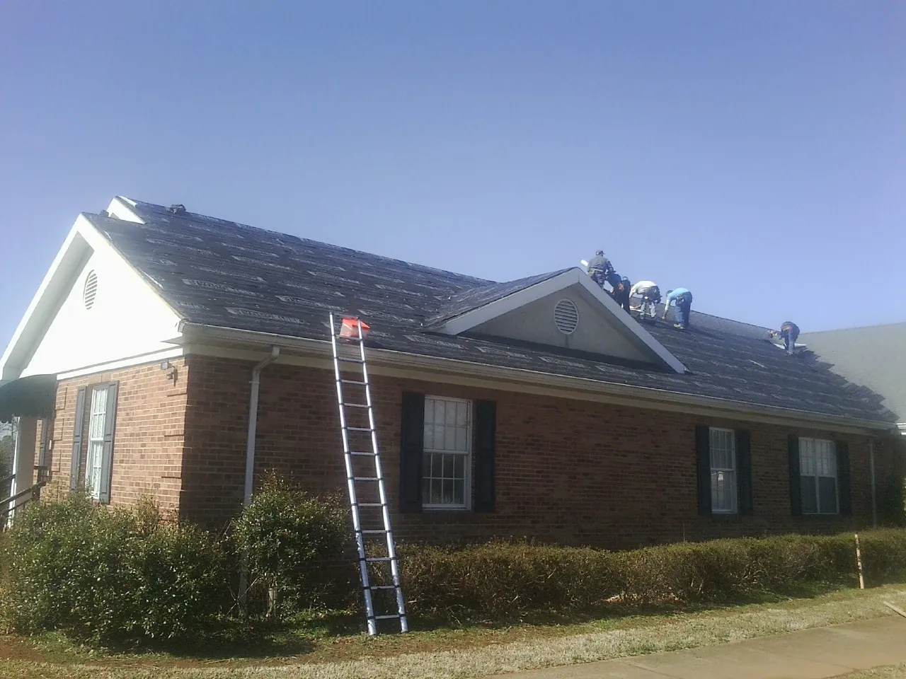 Crew tearing shingles off a brick ranch roof with a ladder set — Emergency Roof Repair work by our crew in Dunsmuir