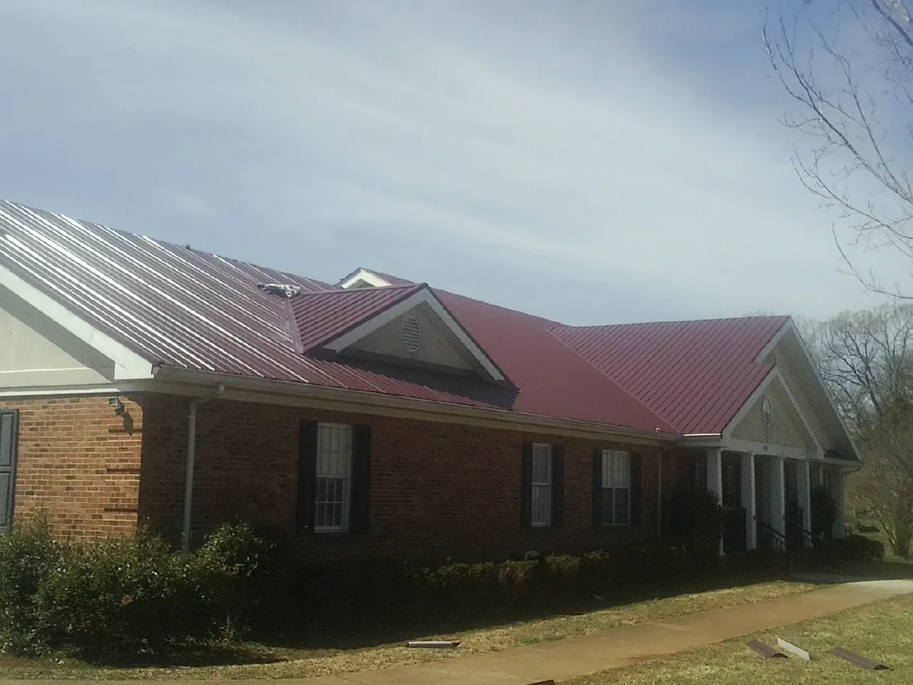 Red metal roof with gabled entries on a long brick building, from a Hail Damage Roof Repair job in Dunsmuir