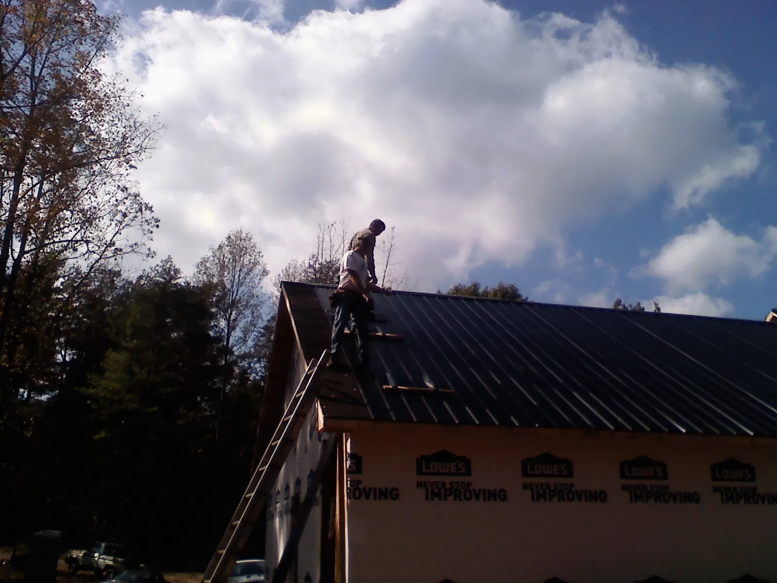 Roofer fastening dark metal panels high against a cloudy sky, from a Roof Inspection job in Dunsmuir